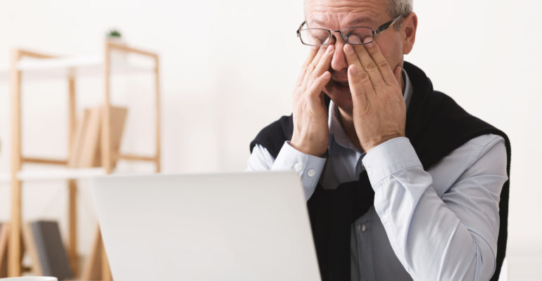 Hard day. Elderly man feeling tired, working on laptop